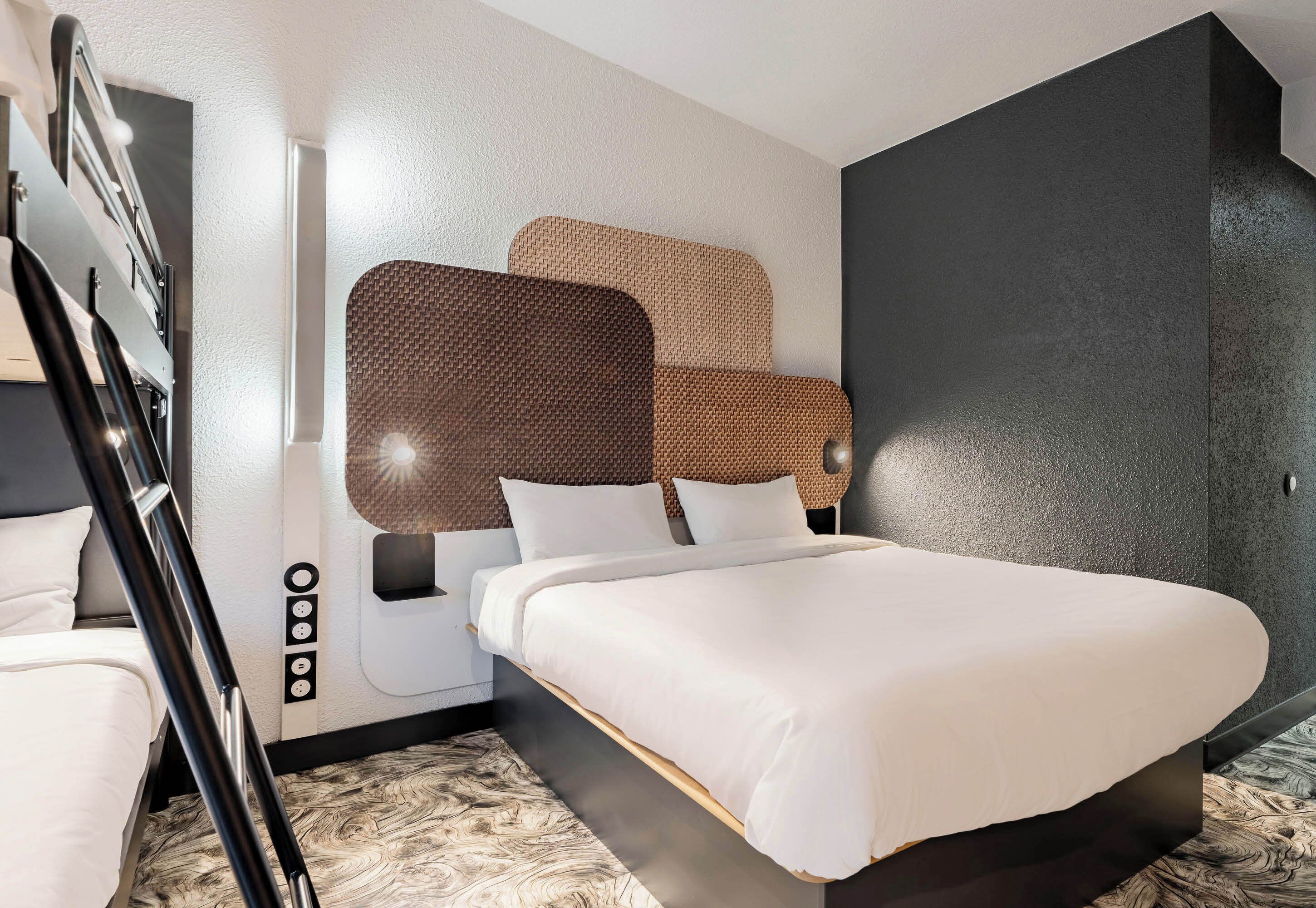 Een moderne hotelkamer met een groot bed, een houten hoofdeinde en een accentmuur in het zwart.