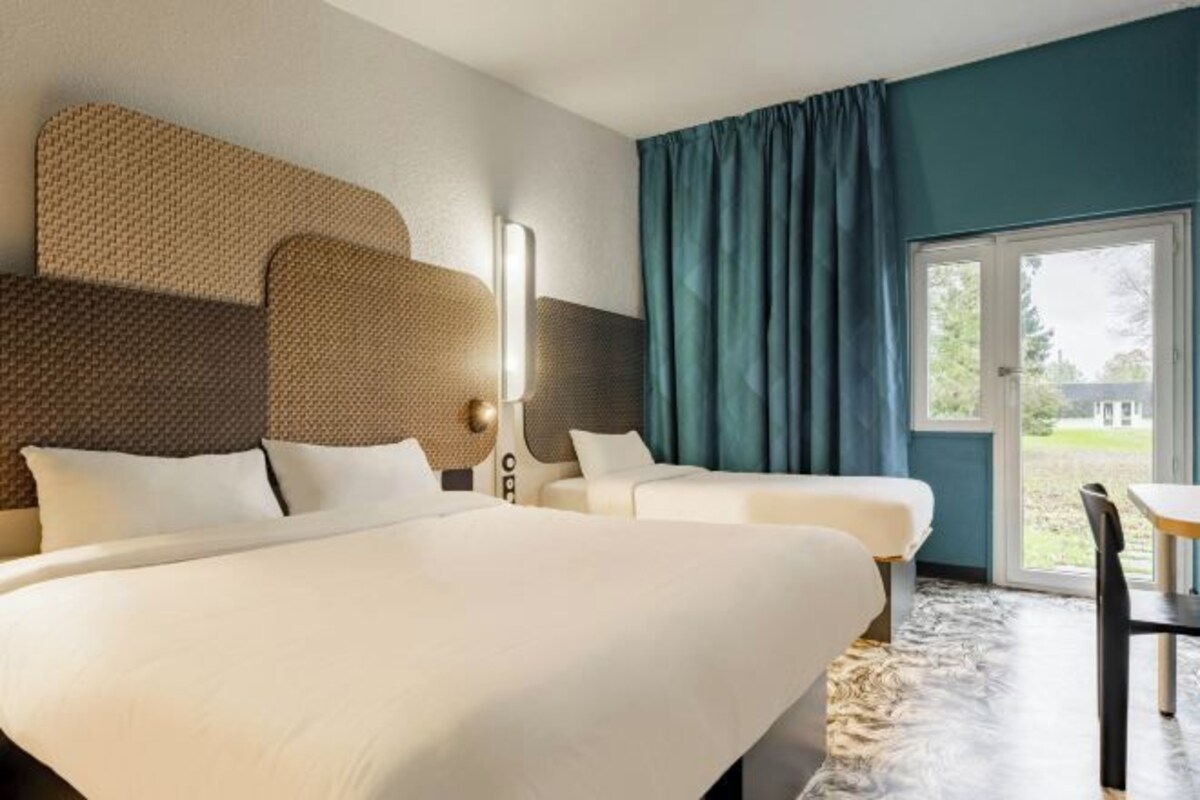 A hotel room with a large bed, two smaller beds, a dining table, and a view of the outdoors.