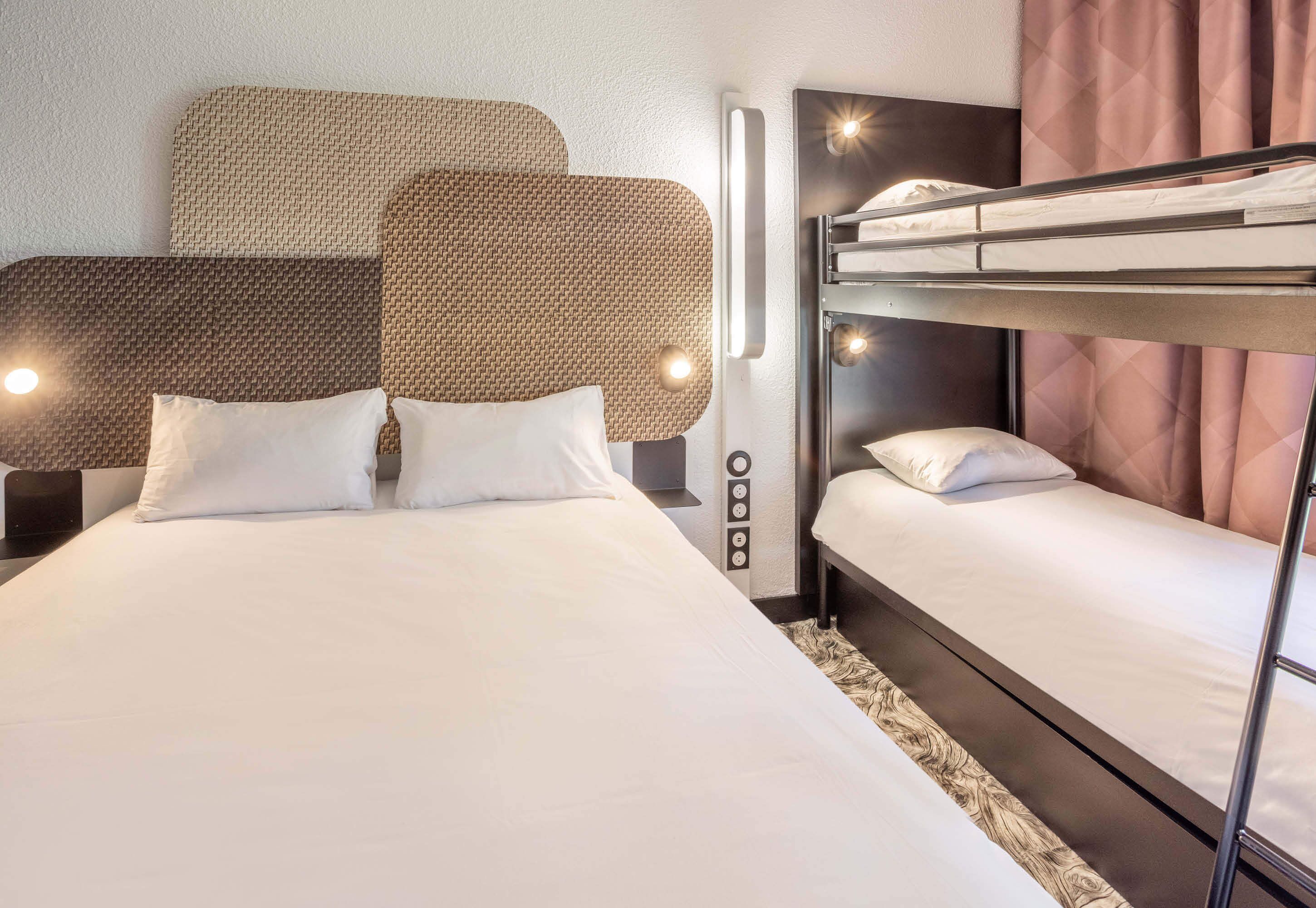 A hotel room with a large bed, a bunk bed, and a bedside table with a lamp.