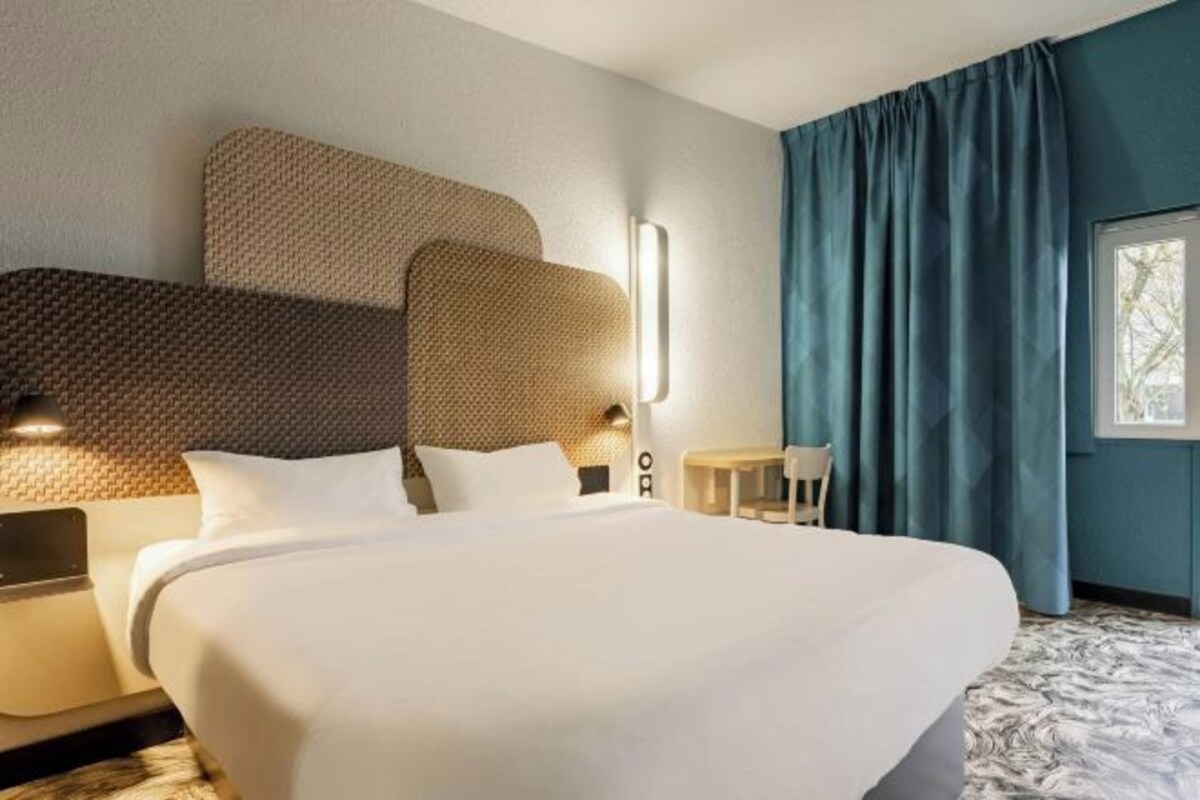 Een hotelkamer met een groot bed, een hoofdbord, nachtkastjes en een raam met gordijnen.