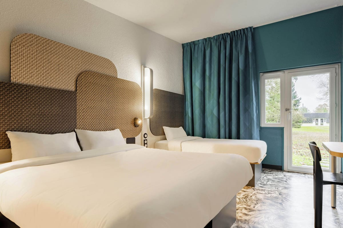 Une chambre d’hôtel avec deux lits, une grande fenêtre avec des rideaux, une table et une chaise.