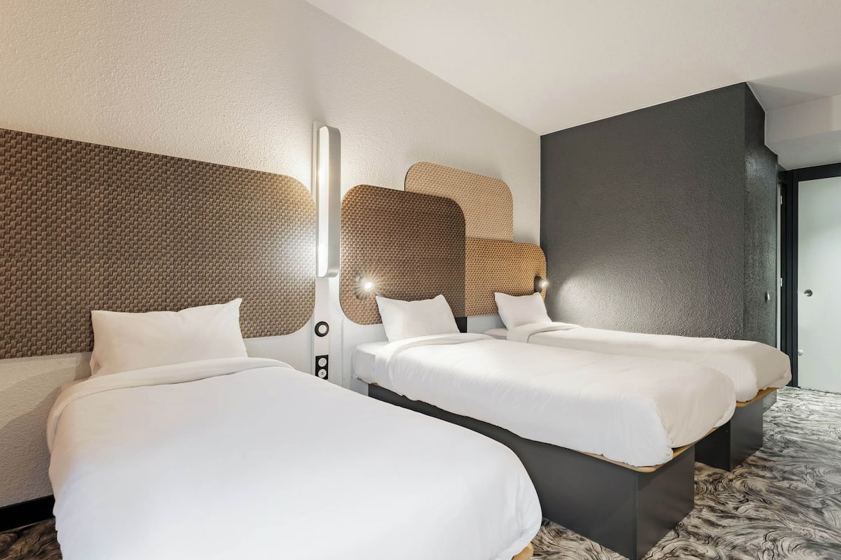 Une chambre d’hôtel avec deux lits, un mur à texture, un luminaire moderne et un mur d’accent de couleur foncée.