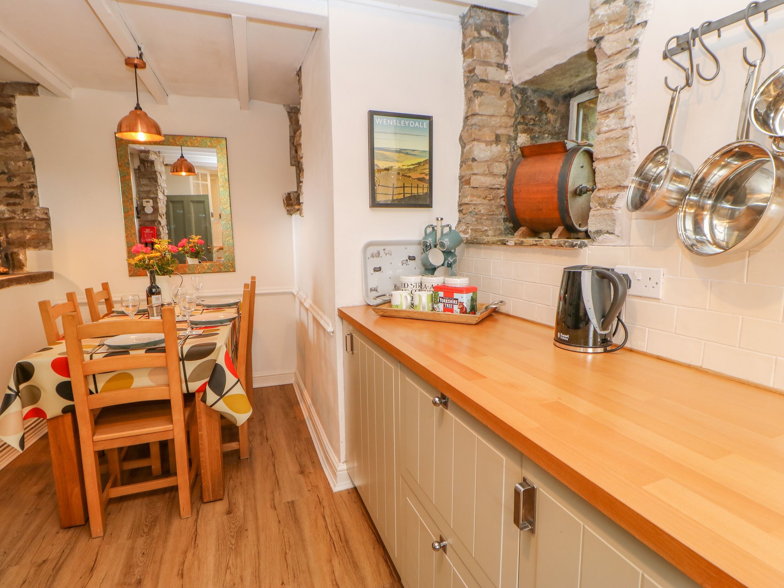 A kitchen with wooden cabinets, a stone wall, and hanging pots.