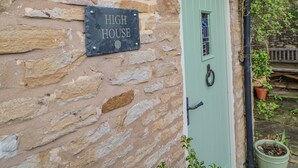 Un mur de pierre sur lequel est apposée une plaque indiquant « HIGH HOUSE », ainsi qu’une porte verte dotée d’une fenêtre et d’une sonnette.