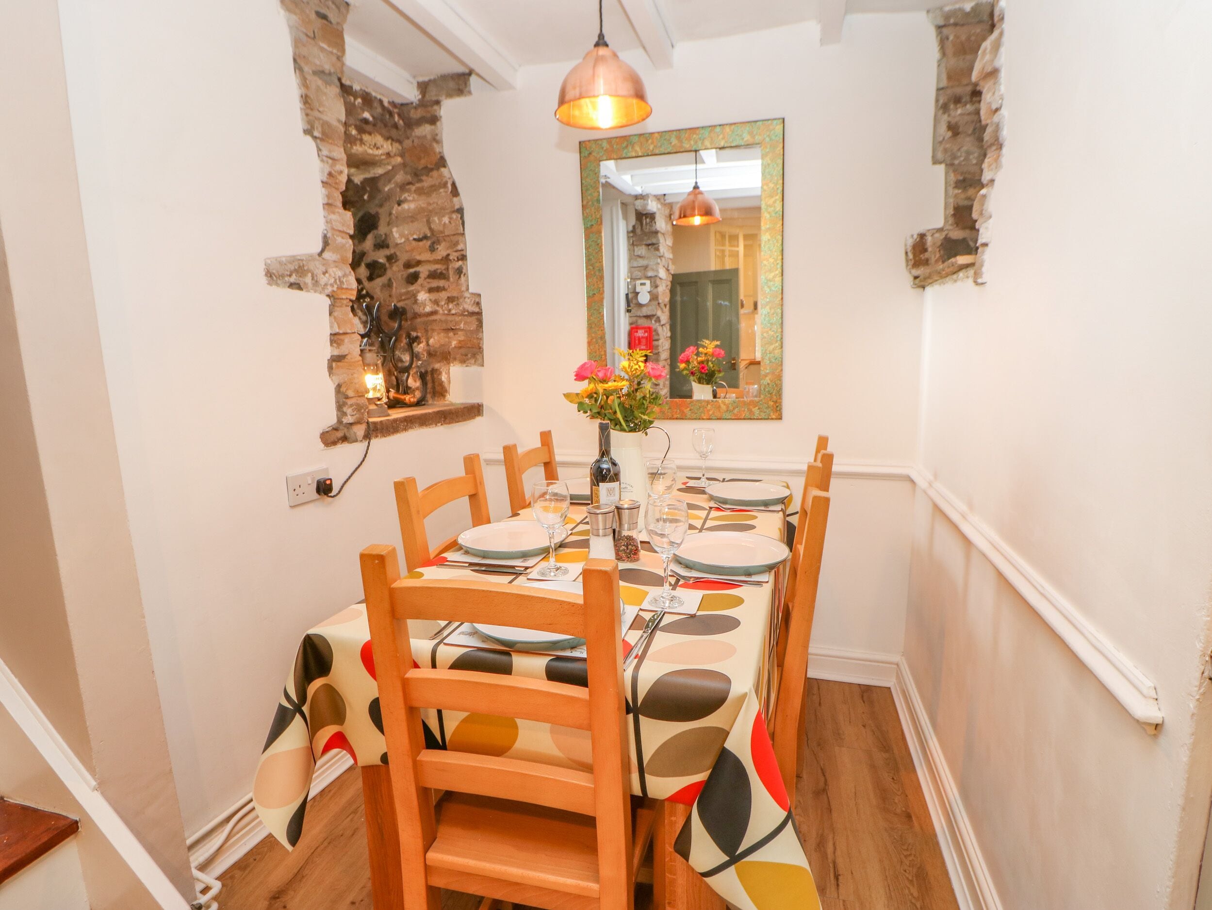Comedor con pared de ladrillo, sillas de madera, una mesa para cuatro personas y una lámpara colgante.