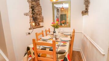 Comedor con pared de ladrillo, sillas de madera, una mesa para cuatro personas y una lámpara colgante.