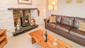 Un salon chaleureux avec une cheminée en pierre, un canapé en cuir marron et une table basse en bois sur laquelle se trouvent une bouteille et un verre.