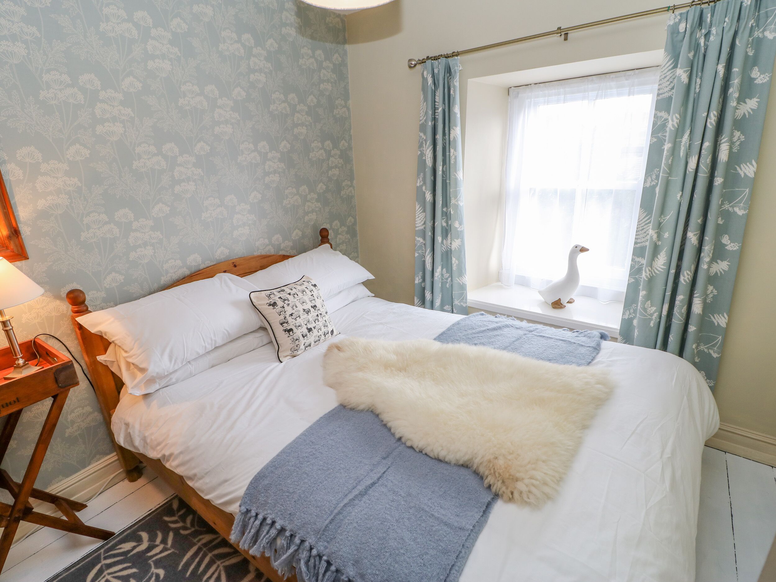 A neatly made bed with a fluffy white throw, a pillow with a pattern, and a blue blanket.