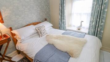 A neatly made bed with a fluffy white throw, a pillow with a pattern, and a blue blanket.
