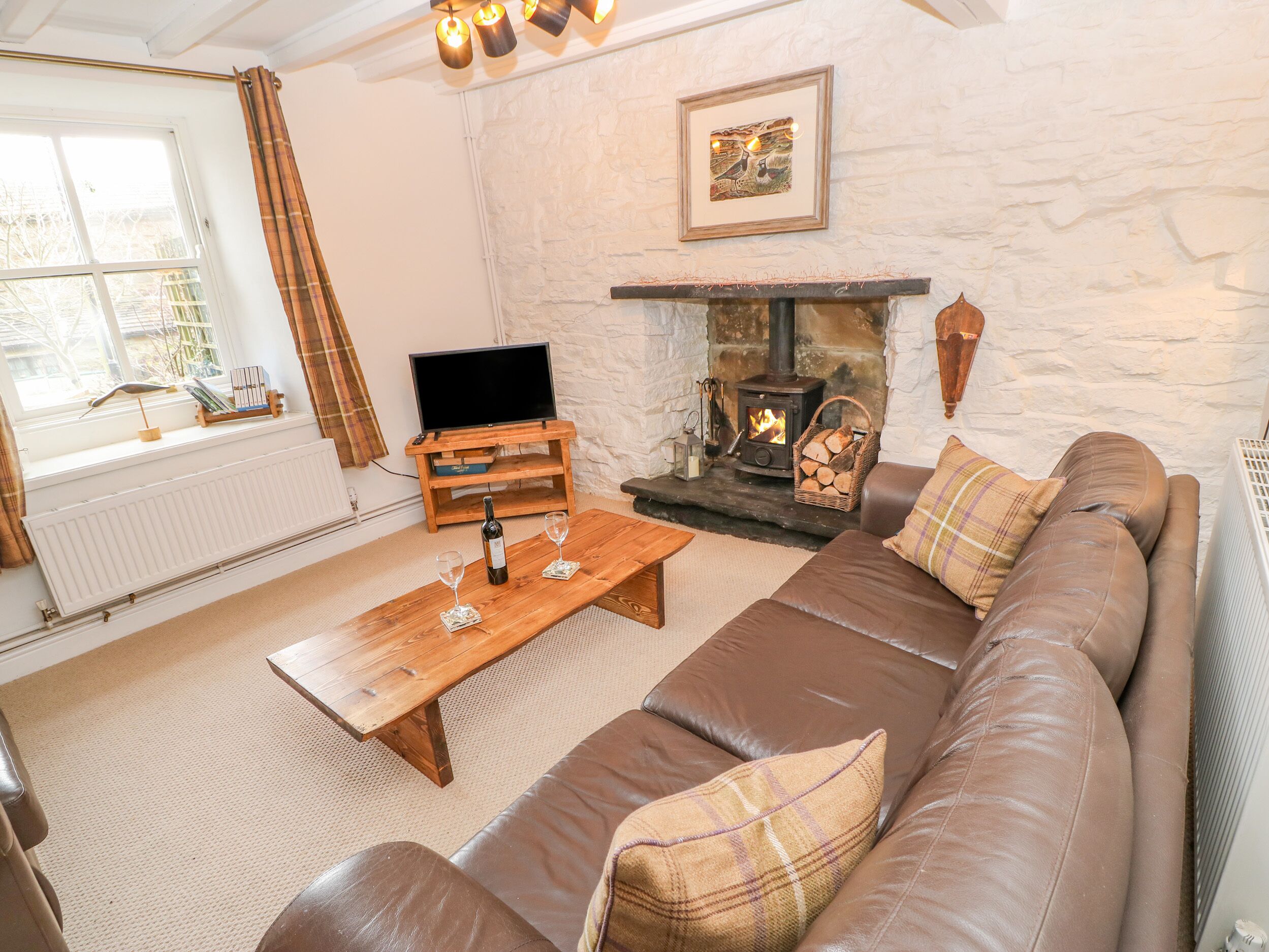 A cozy living room with a stone fireplace, a brown leather sofa, a wooden coffee table, and a television on a wooden stand.