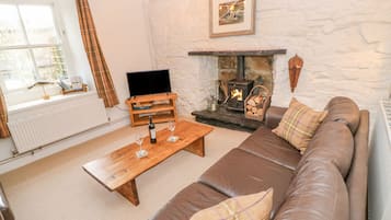 A cozy living room with a stone fireplace, a brown leather sofa, a wooden coffee table, and a television on a wooden stand.