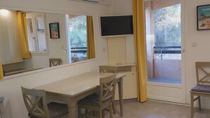 A room with a dining table, chairs, a TV, a window with curtains, and a poster on the wall.