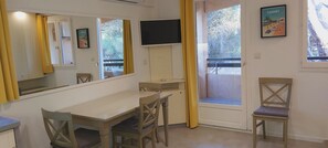 A room with a dining table, chairs, a TV, a window with curtains, and a poster on the wall.
