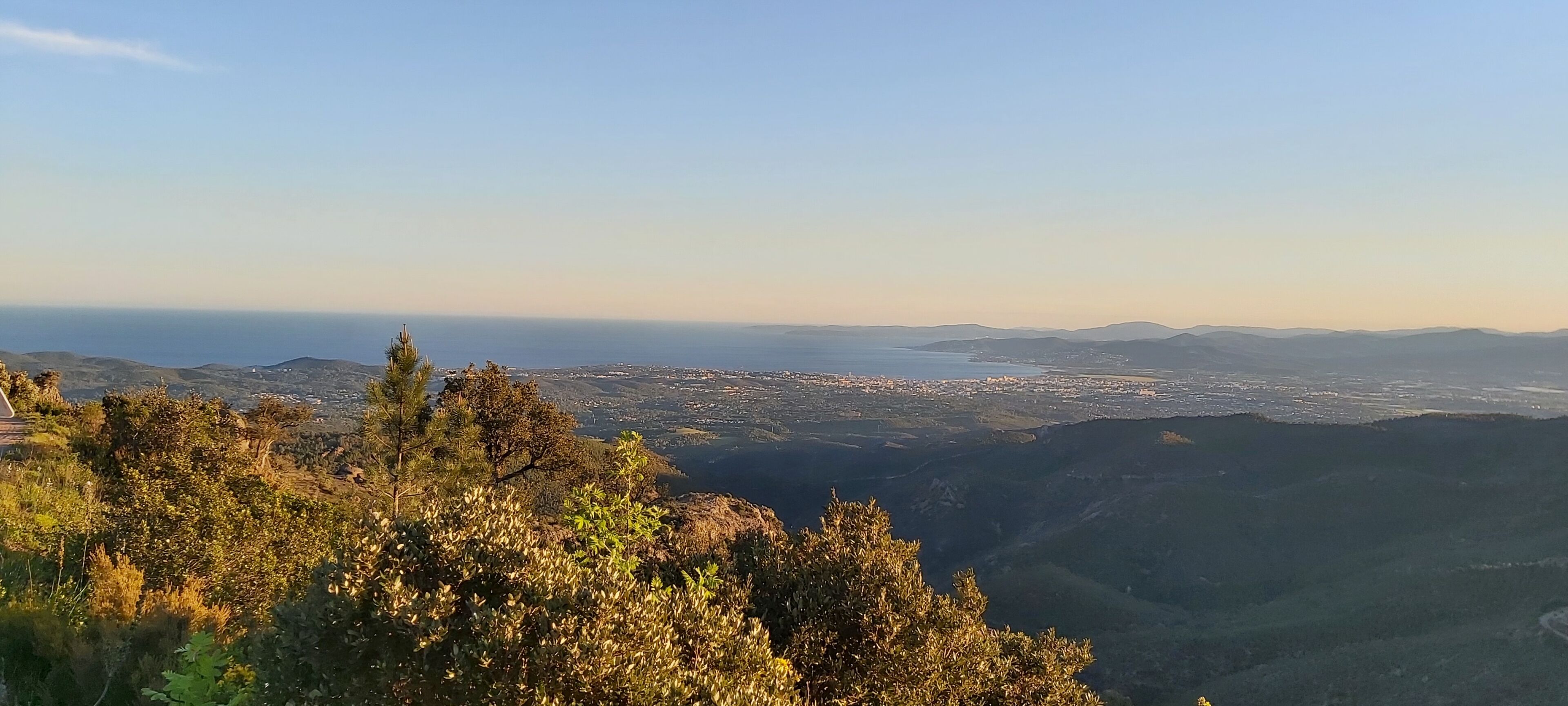 A panoramic view of a coastal city from a high vantage point, featuring a mix of urban and natural landscapes.