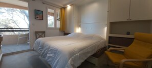 A bedroom with a bed, a chair, a window with curtains, and a door.