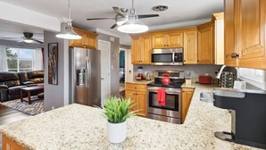 Une cuisine moderne dotée de plans de travail en granit, d’appareils électroménagers en acier inoxydable, d’armoires en bois et d’un ventilateur de plafond.