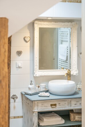 Une salle de bain avec un lavabo blanc, un miroir doté d’un cadre orné et des éléments décoratifs en forme de cœur sur les murs.