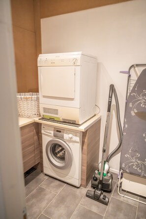 A compact laundry area with a washing machine, stacked dryer, and a vacuum cleaner.