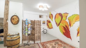 Une pièce ornée d’une grande fresque murale, d’un tonneau en bois, d’un tapis à motifs et d’un paravent décoratif où sont disposés des magazines.