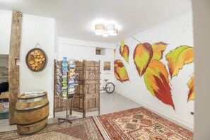 A room with a large wall mural, a wooden barrel, a patterned rug, and a decorative screen with magazines.