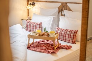 A bed with white linens, red and white checkered pillows, a tray with croissants, coffee cups, and orange juice.