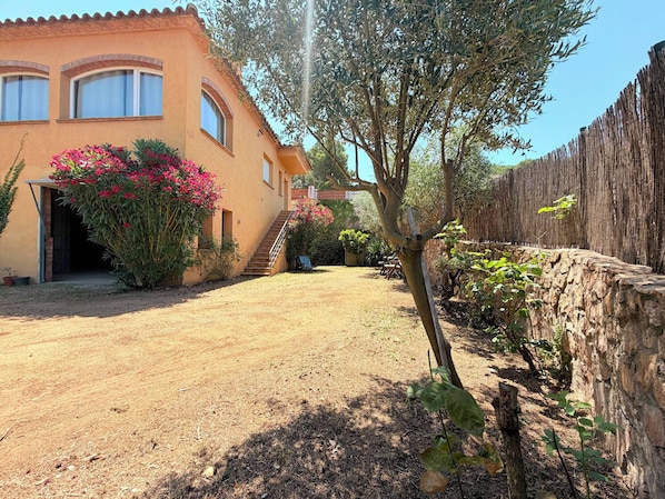 Un edificio con una escalera que conduce a una puerta, rodeado de un jardín con plantas en flor y un muro de piedra.