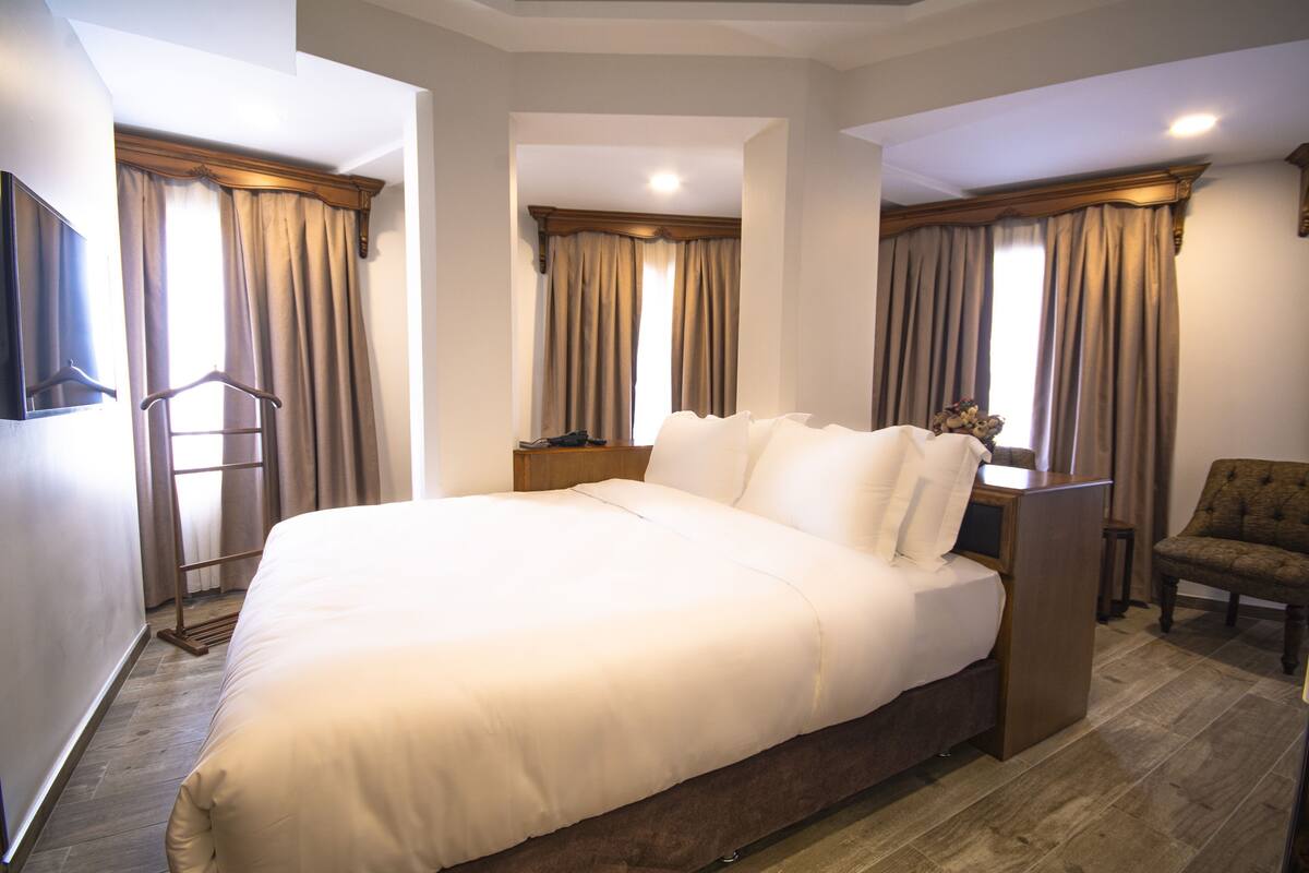 A hotel room with a large bed, a chair, a nightstand, and a wardrobe.