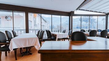 Um restaurante com janelas amplas, mesas com toalhas brancas e cadeiras pretas.