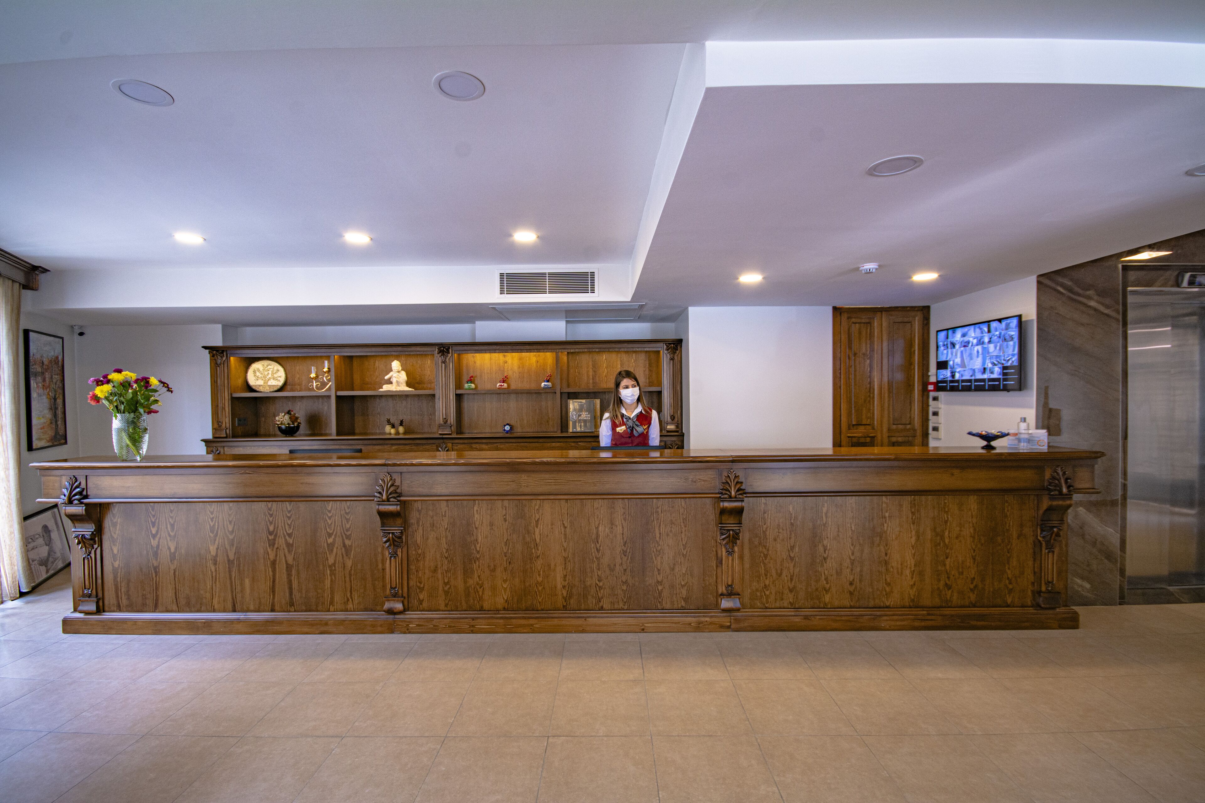 A reception desk with a wooden finish, a vase with flowers, and a television mounted on the wall.