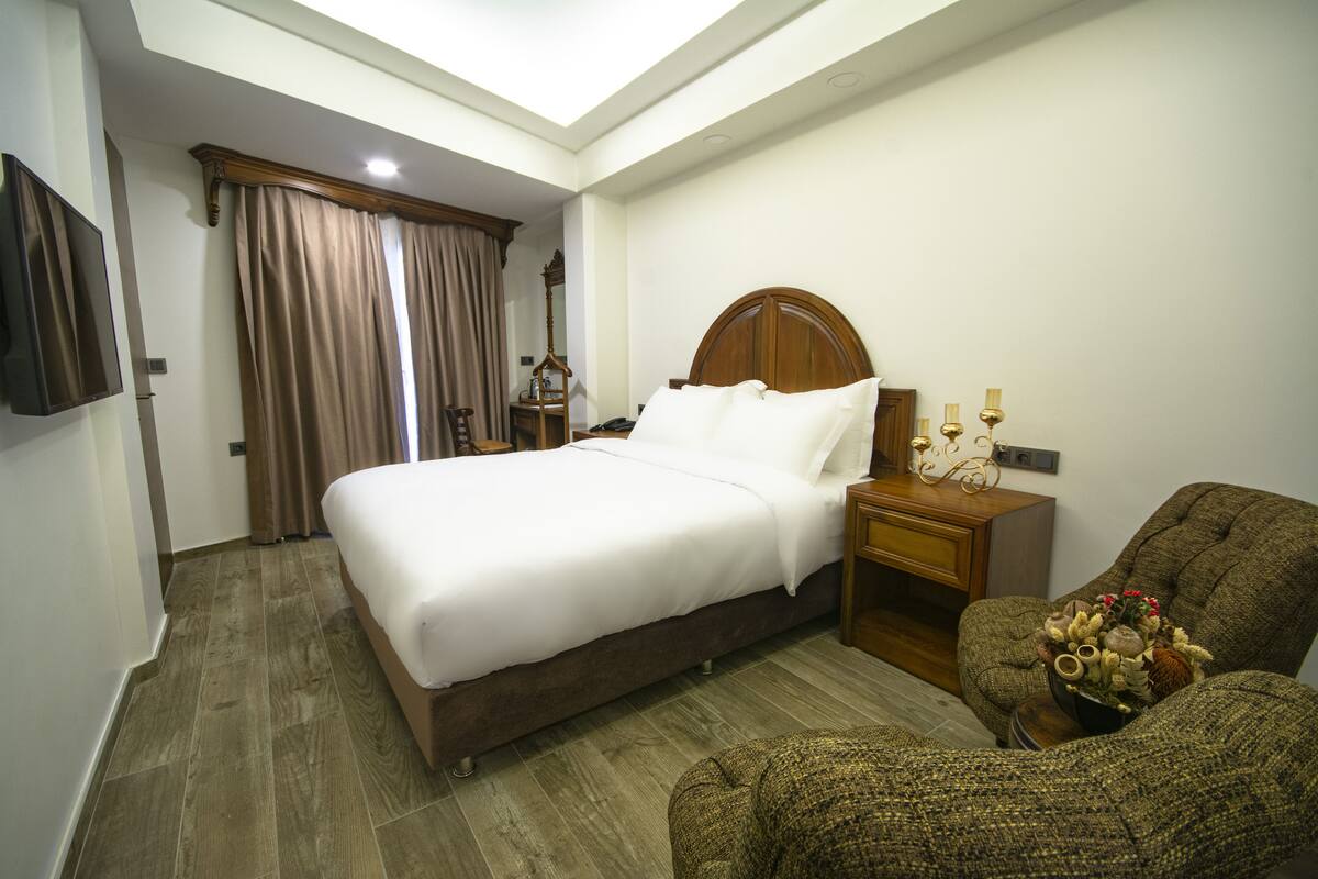 A hotel room with a large bed, a wooden nightstand, a chair, and a TV mounted on the wall.