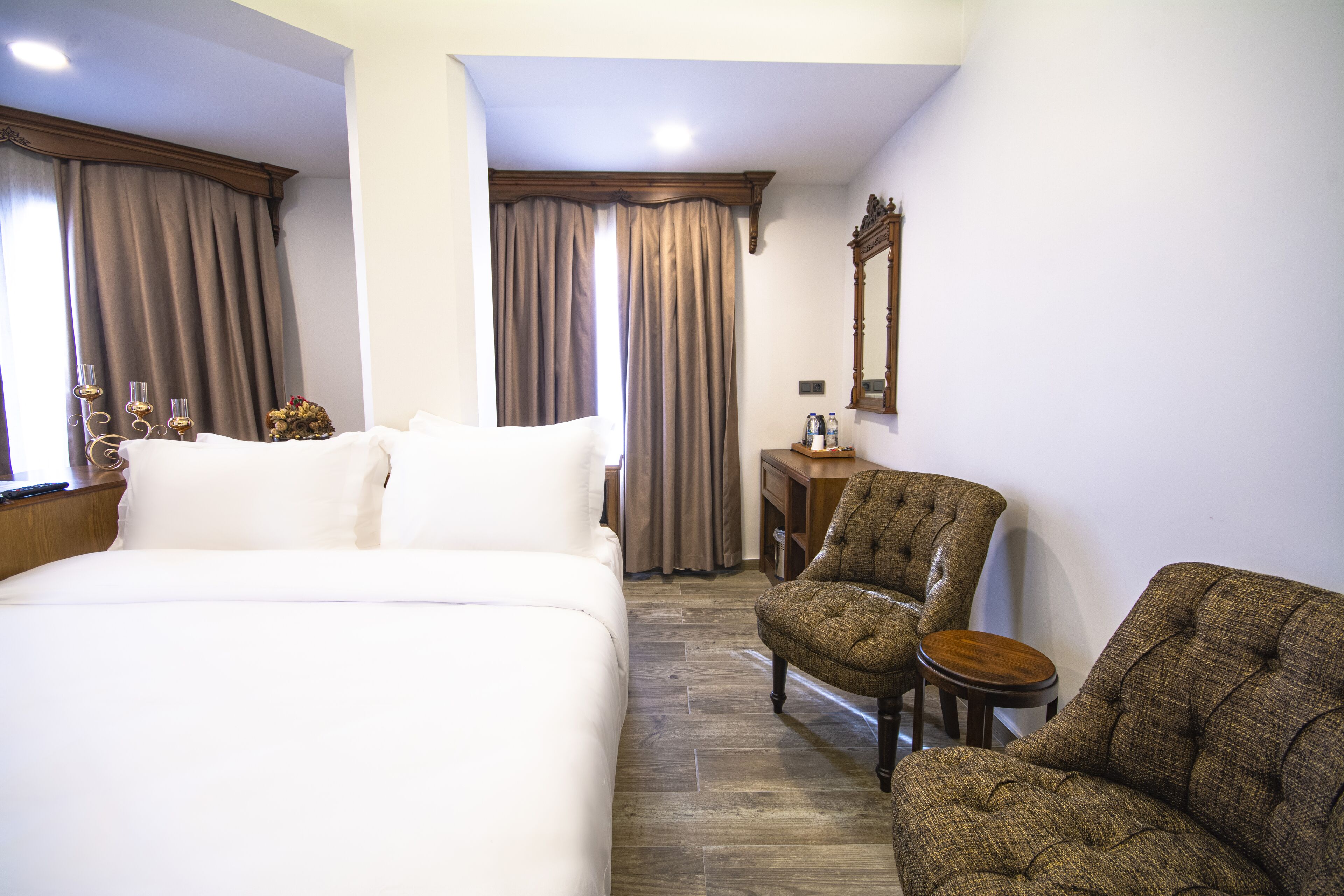 A hotel room with a large bed, two armchairs, a small table, and a mirror on the wall.