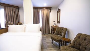 A hotel room with a large bed, two armchairs, a small table, and a mirror on the wall.