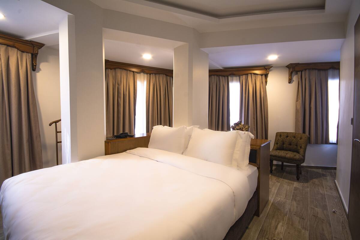 A hotel room with a large bed, a chair, a desk, and curtains.