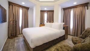 Um quarto com uma cama grande, cabeceira de madeira, uma mesa de cabeceira de madeira, uma escada de madeira e um sofá marrom.