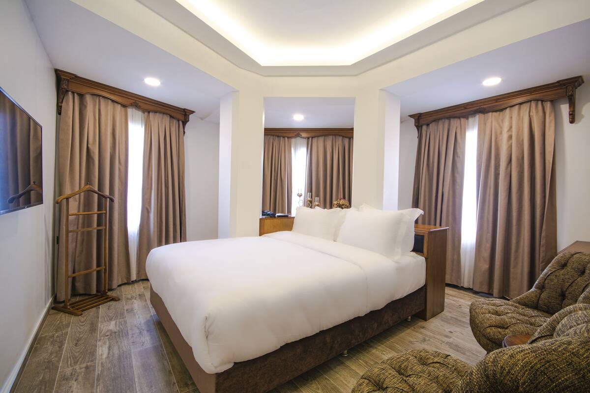 A bedroom with a large bed, wooden headboard, a wooden nightstand, a wooden ladder, and a brown sofa.