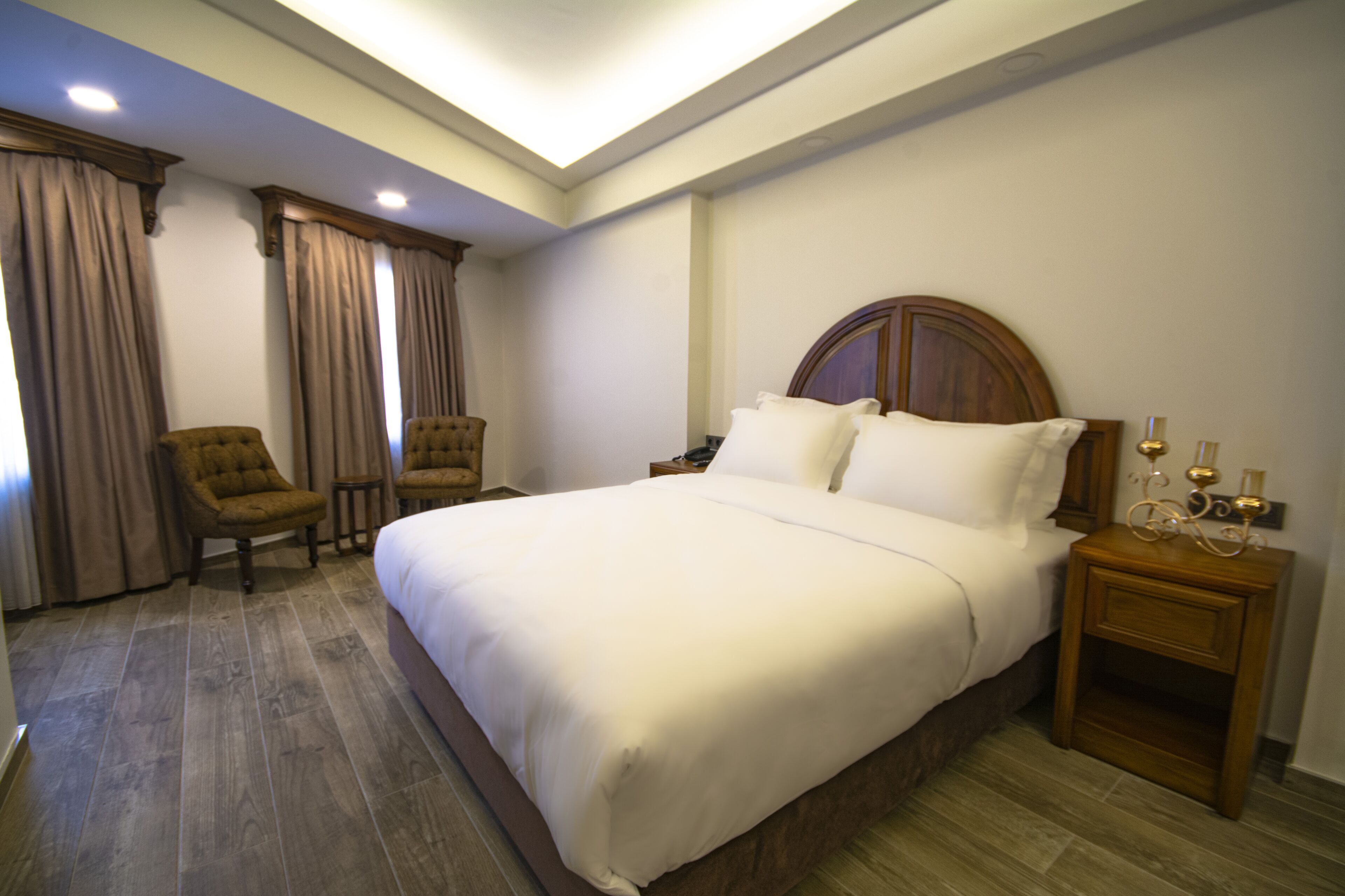 A hotel room with a large bed, two armchairs, a wooden nightstand, and a ceiling light.
