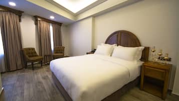 A hotel room with a large bed, two armchairs, a wooden nightstand, and a ceiling light.