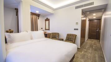 A hotel room with a large bed, two armchairs, a small table, a mirror, and a door leading to another room.