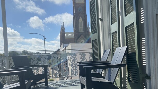 Een veranda met uitzicht op een kerktoren, tuinmeubels en een mok met een patroon.