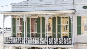 Een gebouw met twee verdiepingen, versierde balkons en groene luiken.