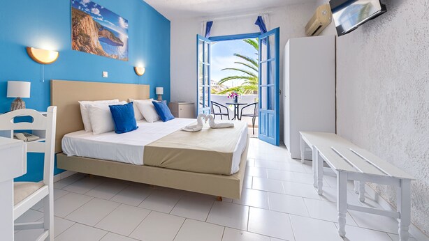 A bedroom with a bed, bedside tables, a TV, and a balcony with a view of the sea. - Bluu Bahari EE (Karpathos)