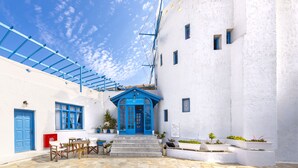A white building with a blue door and windows, a covered patio area, and potted plants. - Bluu Bahari EE (Karpathos)