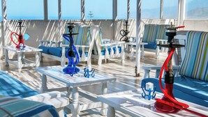 A sunlit outdoor seating area with white furniture and striped cushions, overlooking a scenic view. - Bluu Bahari EE (Karpathos)