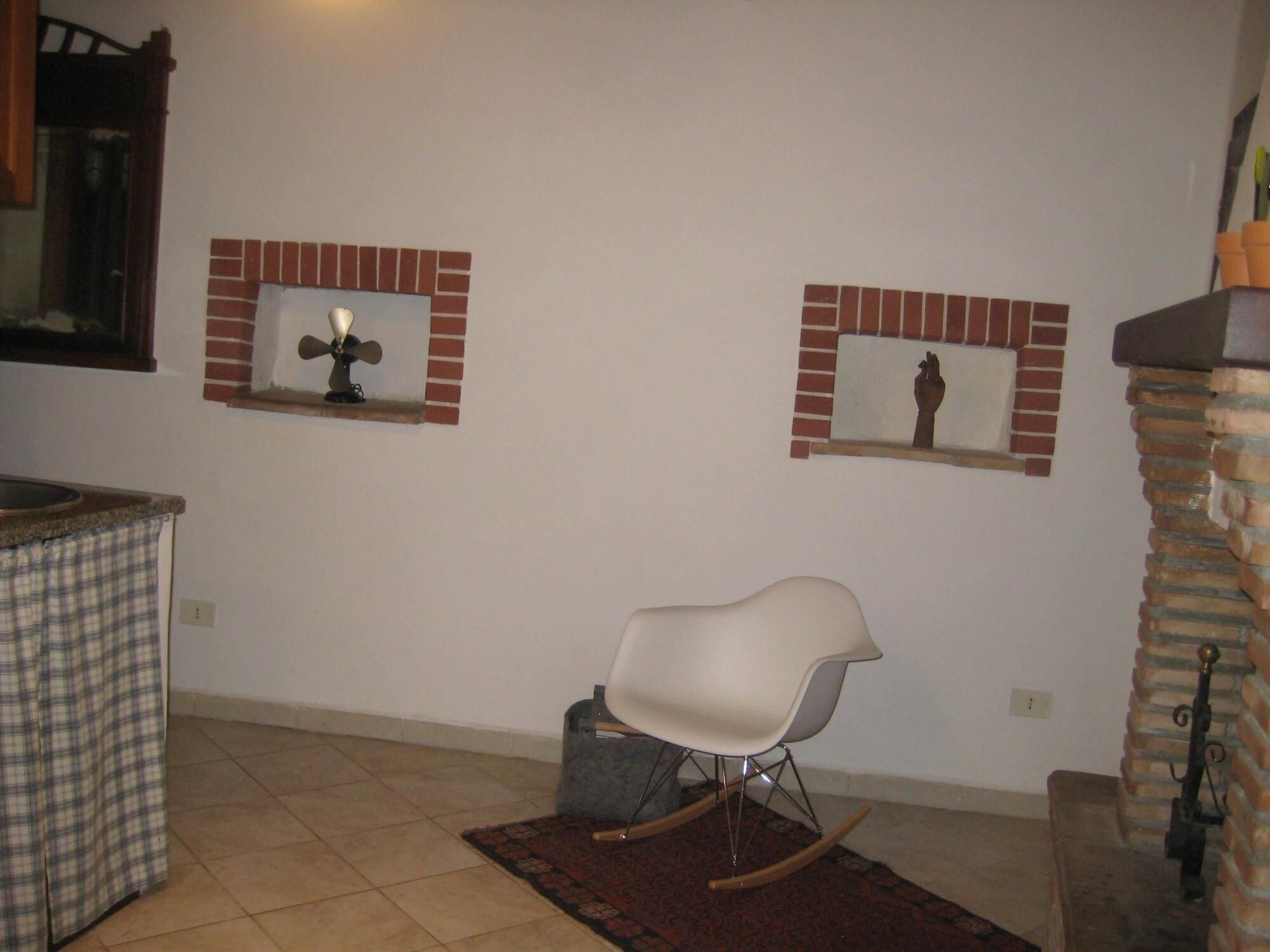 Una cocina con un mantel a cuadros sobre el lavadero, una mecedora blanca y dos repisas de chimenea de ladrillo con adornos.