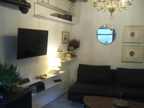 A living room with a flat-screen TV, a sofa, a coffee table, and a chandelier.