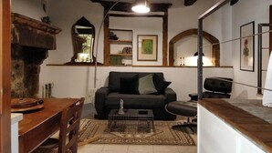 A cozy living room with a wooden dining table, a black sofa, and a small black office chair. There is a wooden cabinet on the left and a mirror above the sofa. - Casa Messi - Casa Messi a Vicolo Della Rivolta 25 Apt 5 (Pitigliano)