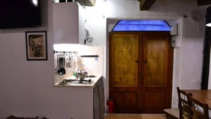 Une cuisine de taille réduite, équipée d’une cuisinière à gaz, de ustensiles suspendus et d’une porte en bois.