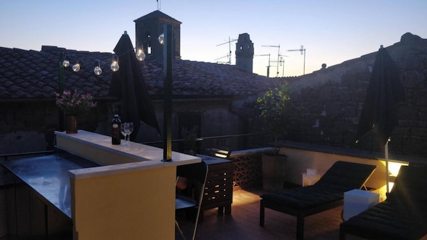 Une terrasse sur le toit dotée d’une piscine, de chaises longues, d’un espace bar avec des bouteilles et des verres, et offrant une vue sur les bâtiments environnants.