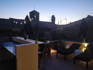 Une terrasse sur le toit dotée d’une piscine, de chaises longues, d’un espace bar avec des bouteilles et des verres, et offrant une vue sur les bâtiments environnants.