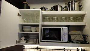 Une cuisine équipée d’un four à micro-ondes, d’étagères avec des bocaux en verre, de l’assiette et des ustensiles de cuisine.